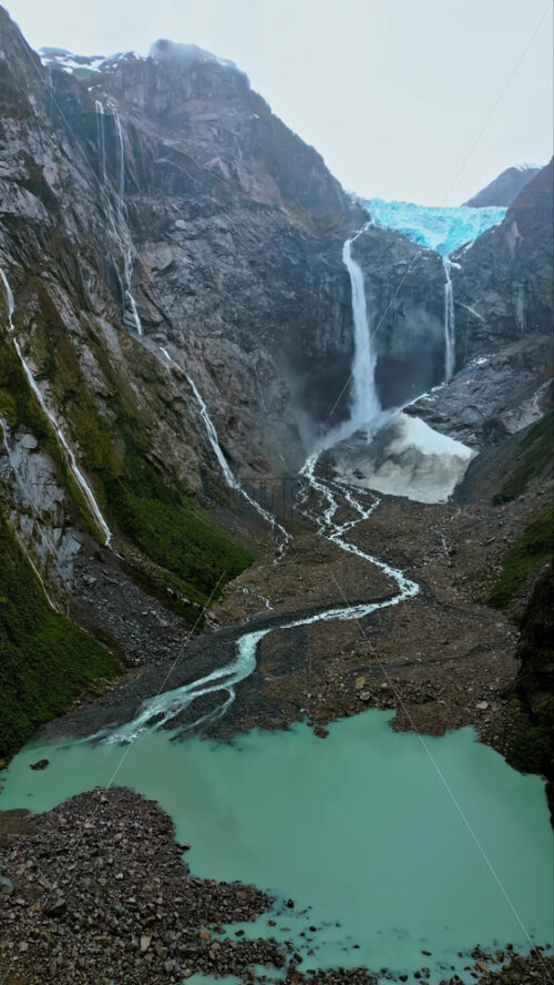 Video - Aerial drone view of a glacier waterfall cascading down steep cliffs into turquoise pools in Patagonia. Vertical