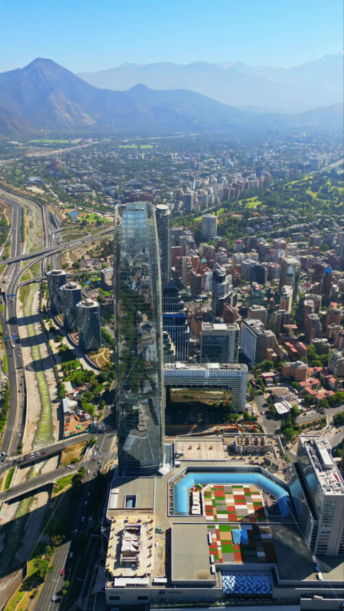 Video - Aerial drone view over Santiago's financial district with the Costanera Center and green areas visible on a clear day. Vertical
