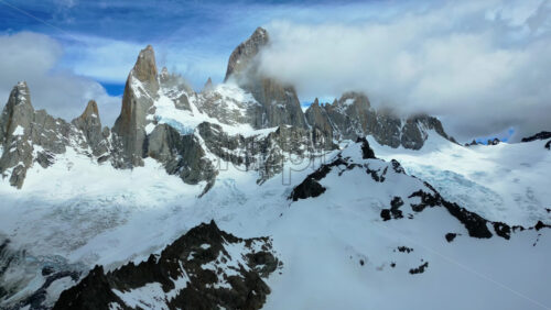 Video - Aerial drone view of the dramatic granite peaks of Fitz Roy partially covered by clouds with glaciers stretching across the slopes
