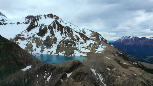 Video - Aerial drone view the vibrant blue, high altitude lake surrounded by snow patches and rocky slopes