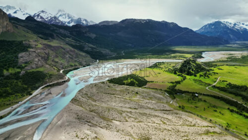 Video - Aerial drone view of winding rivers and green plains stretching between mountains in Patagonia under cloudy skies