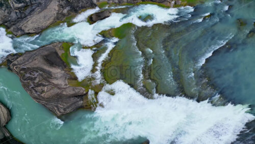 Video - Aerial drone view of fast flowing glacial river cutting through rocky terrain, showing vivid turquoise water and white foam