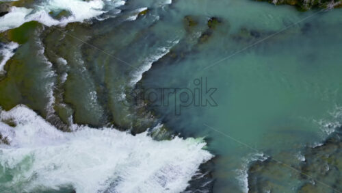 Video - Aerial drone view of fast flowing glacial river cutting through rocky terrain, showing vivid turquoise water and white foam