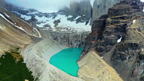 Video - Aerial drone view of the iconic Torres del Paine towers rising above a turquoise lake surrounded by snow and steep cliffs