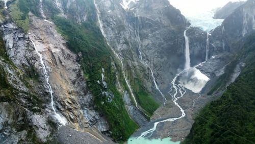 Video - Aerial drone view of the stunning Ventisquero Colgante glacier waterfall cascading down steep cliffs surrounded by lush green forest in slow motion