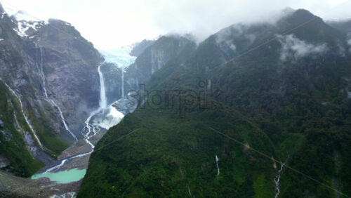 Video - Aerial drone view of the stunning Ventisquero Colgante glacier waterfall cascading down steep cliffs surrounded by lush green forest in slow motion