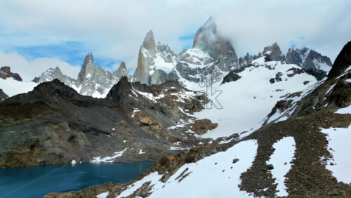 Video - Aerial drone view of the dramatic granite peaks of Fitz Roy partially covered by clouds with glaciers stretching across the slopes in slow motion