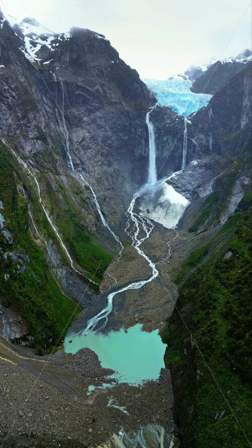 Video - Aerial drone view of a glacier waterfall cascading down steep cliffs into turquoise pools in Patagonia. Vertical