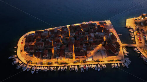 Video – Aerial drone view narrow streets and boats docked around the entire curved coastline of the old town of Tribunj Island at night - Starpik Stock