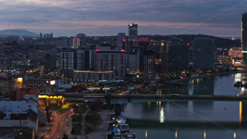 Video – Aerial drone view of Belgrade Waterfront at blue hour, showcasing the illuminated Sava River, modern skyline, Ada Bridge, and colorful reflections on the water - Starpik Stock
