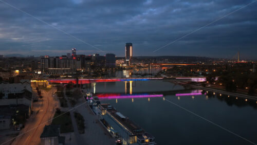 Video – Aerial drone view of Belgrade Waterfront at blue hour, showcasing the illuminated Sava River, modern skyline, Ada Bridge, and colorful reflections on the water - Starpik Stock