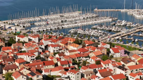 Video – Aerial drone view of Biograd’s residential area near the marina, showing clusters of red roofed homes with the harbor and anchored boats visible in the background. Biograd na Moru, Croatia - Starpik Stock