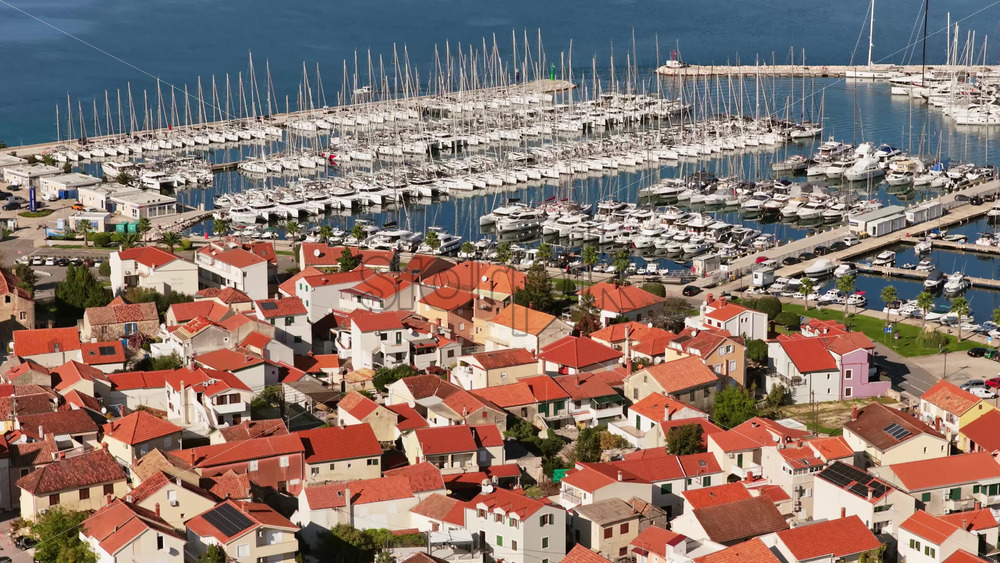 Video – Aerial drone view of Biograd’s residential area near the marina, showing clusters of red roofed homes with the harbor and anchored boats visible in the background. Biograd na Moru, Croatia - Starpik Stock