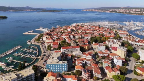 Video – Aerial drone view of Biograd’s residential area near the marina, showing clusters of red roofed homes with the harbor and anchored boats visible in the background. Biograd na Moru, Croatia - Starpik Stock