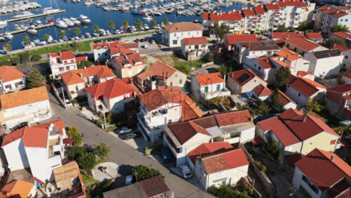 Video – Aerial drone view of Biograd’s residential area near the marina, showing clusters of red roofed homes with the harbor and anchored boats visible in the background. Biograd na Moru, Croatia - Starpik Stock