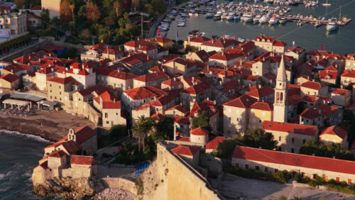 Video – Aerial drone view of Budva Old Town, focusing on the marina, the church tower, and the compact stone houses. Montenegro - Starpik Stock