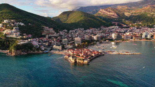 Video – Aerial drone view of Budva, showing the Old Town surrounded by modern buildings and the lush mountains. Montenegro - Starpik Stock