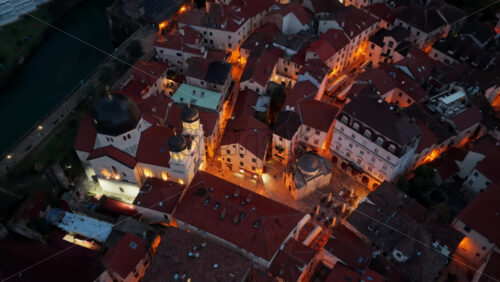 Video – Aerial drone view of Kotor’s Old Town during blue hour, featuring the central church, red rooftops, and stone streets softly illuminated by warm streetlights - Starpik Stock