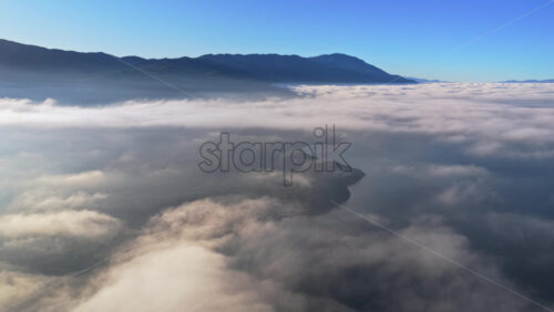 Video – Aerial drone view of a Galichica mountain ridge rising above a sea of clouds, with soft layers of fog covering the valley below - Starpik Stock