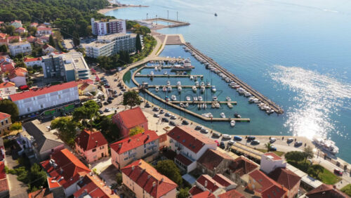 Video – Aerial drone view of a coastal neighborhood with red roofed houses, narrow streets, and a small marina along the shoreline. Biograd na Moru, Croatia - Starpik Stock