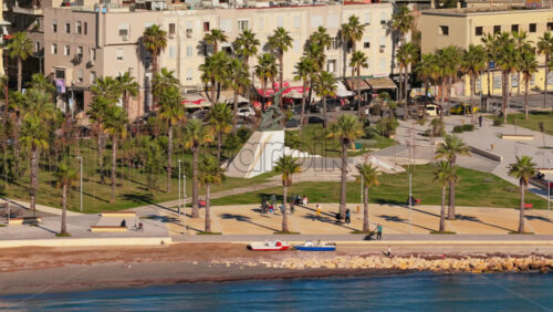 Video – Aerial drone view of a coastal promenade lined with tall palm trees, benches, and walking paths. Montenegro - Starpik Stock