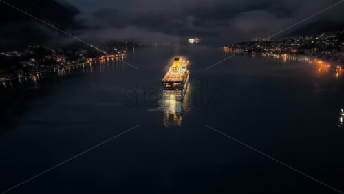 Video – Aerial drone view of a cruise ship moving slowly through a dark and misty bay at night, with faint lights of surrounding towns reflecting on the water near the Bay of Kotor - Starpik Stock