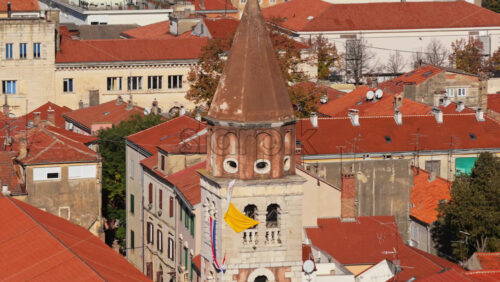 Video – Aerial drone view of a distinctive church bell tower with a red brown conical roof and stone base in Zadar, Croatia - Starpik Stock