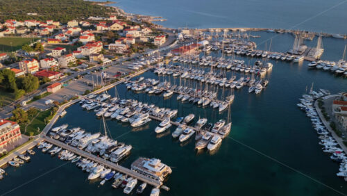 Video – Aerial drone view of a large marina filled with yachts and sailboats, bordered by a coastal town with red roofed homes. Tribunj, Croatia - Starpik Stock
