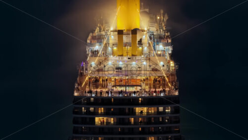 Video – Aerial drone view of a massive cruise ship, brightly lit with warm lights, as passengers enjoy its outdoor decks at night - Starpik Stock