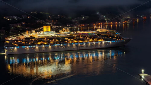 Video – Aerial drone view of a massive cruise ship, brightly lit with warm lights, as passengers enjoy its outdoor decks at night - Starpik Stock