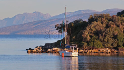 Video – Aerial drone view of a sailboat anchored in Ksamil Bay, surrounded by rocky shores, lush vegetation, and distant mountains - Starpik Stock