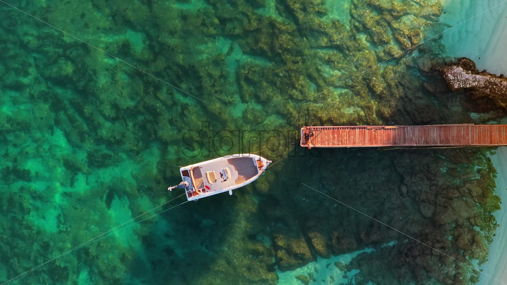Video – Aerial drone view of a small white boat moored to a wooden pier above the transparent, emerald colored water of Ksamil - Starpik Stock