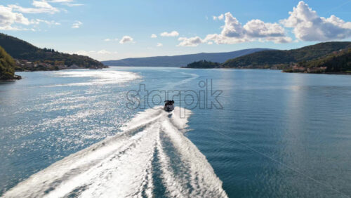 Video – Aerial drone view of a speedboat leaving white trails on the calm water of the bay with mountains in the background. Bay of Kotor, Montenegro - Starpik Stock