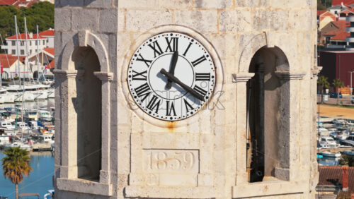 Video – Aerial drone view of a stone clock tower featuring a large white clock face with Roman numerals and the engraving 1859 beneath it. Biograd na Moru, Croatia - Starpik Stock