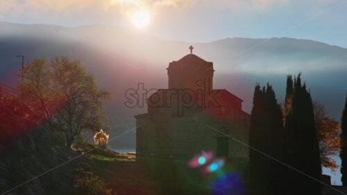 Video – Aerial drone view of a sunrise scene behind St. John at Kaneo, with rays breaking through the clouds and illuminating the church’s silhouette. North Macedonia - Starpik Stock