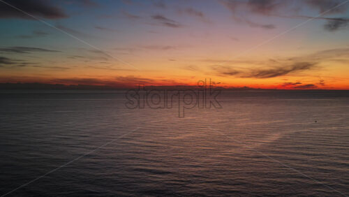Video – Aerial drone view of a vivid sunset over calm open sea, with warm orange and red tones glowing across the horizon. Montenegro - Starpik Stock