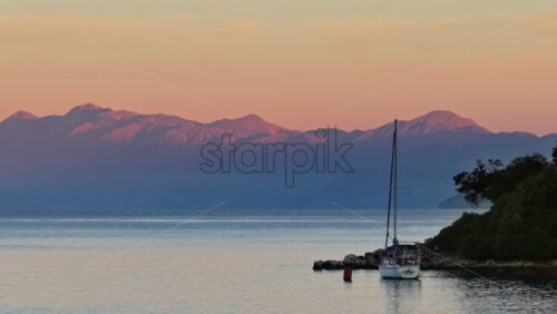 Video – Aerial drone view of a yacht anchored near the rocky shore of Ksamil, Albania, framed by soft mountain silhouettes and calm reflective waters - Starpik Stock
