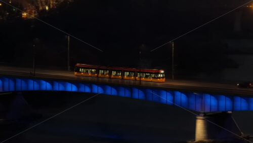 Video – Aerial drone view of a yellow Warsaw tram traveling across the illuminated Swietokrzyski Bridge, with reflections on the Vistula River - Starpik Stock