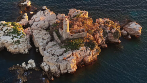 Video – Aerial drone view of an isolated rocky Peristeres Island featuring the old lighthouse ruins, illuminated by golden hour sunlight against the deep blue Adriatic Sea. Greece - Starpik Stock