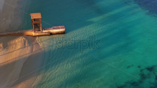 Video – Aerial drone view of an old wooden pier and lookout structure on Ksamil Beach, with clear turquoise waters and soft sand textures - Starpik Stock