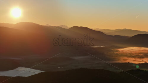 Video – Aerial drone view of morning fog drifting over the agricultural plains, glowing golden under early sunlight. Albania - Starpik Stock