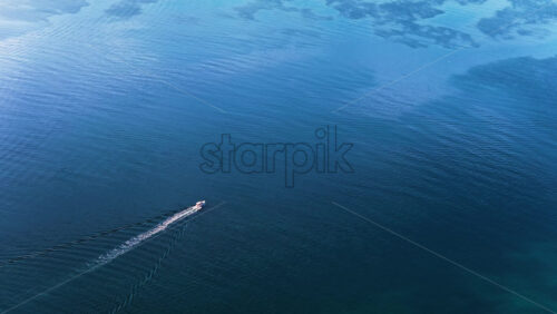Video – Aerial drone view of open blue water with a small motorboat moving across the frame, leaving a long wake behind - Starpik Stock