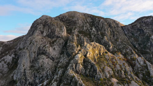 Video – Aerial drone view of rugged grey mountain cliffs, illuminated by soft morning sunlight - Starpik Stock