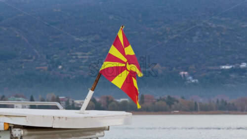 Video – Aerial drone view of the North Macedonian flag waving at the back of a boat, with the blue tones of Lake Ohrid and the distant shoreline behind it - Starpik Stock