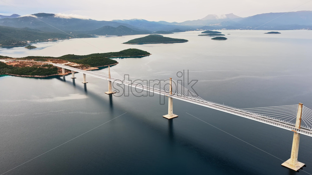Video – Aerial drone view of the Peljesac Bridge near Komarna, Croatia, partially shrouded in low coastal fog with mountains in the background - Starpik Stock