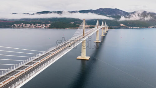 Video – Aerial drone view of the Peljesac Bridge near Komarna, Croatia, partially shrouded in low coastal fog with mountains in the background - Starpik Stock