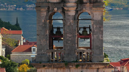 Video – Aerial drone view of the Perast church bell tower’s arches and bells, with rooftops and the shimmering bay in the background. Bay of Kotor, Montenegro - Starpik Stock