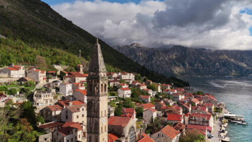 Video – Aerial drone view of the bell tower in Perast rising above traditional stone houses, with the Bay of Kotor and steep mountains visible behind it. Bay of Kotor, Montenegro - Starpik Stock