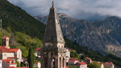 Video – Aerial drone view of the bell tower in Perast rising above traditional stone houses, with the Bay of Kotor and steep mountains visible behind it. Bay of Kotor, Montenegro - Starpik Stock