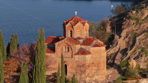 Video – Aerial drone view of the iconic St. John the Theologian Church perched above Lake Ohrid, framed by cypress trees and autumn colors. North Macedonia - Starpik Stock